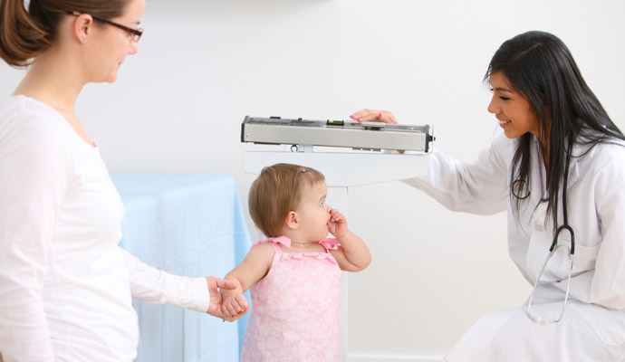 Doctor weighing a small child while mother watches
